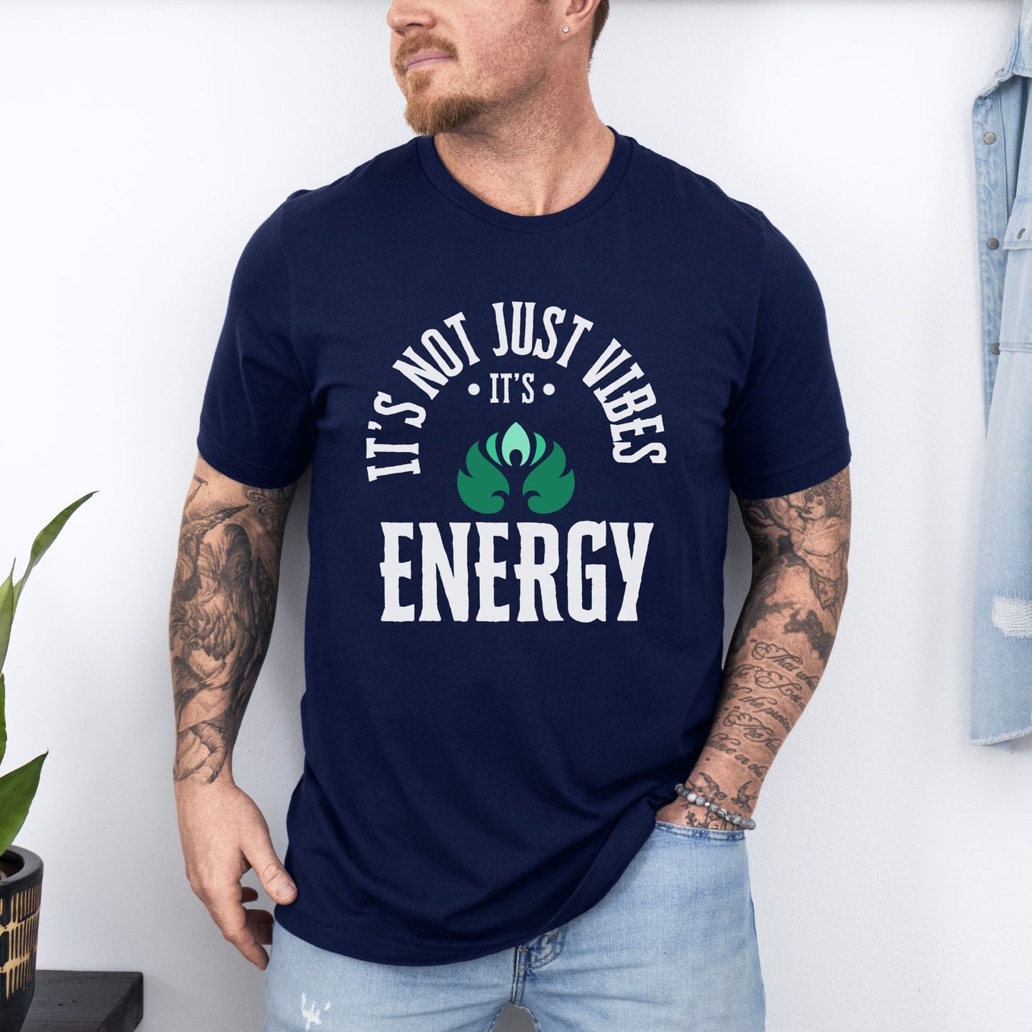 Man wearing a navy blue t-shirt with Its not just vibes its energy text and design, standing against a white wall – Lunar Lightwear conscious clothing